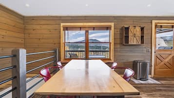 A wooden interior with a long table, chairs, a window with a view, and a door.
