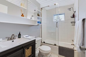 A modern bathroom with a glass-enclosed shower, a white sink with a dark cabinet, and a toilet.