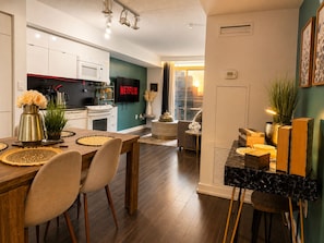 A modern kitchen with a flat-screen TV, a dining area with a wooden table and chairs, and a living space with a sofa and a coffee table. - Luxury Skyline View | 2 Master Suites | CityPlace (Toronto)