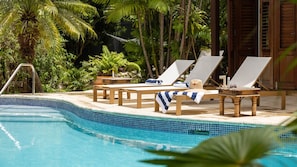 A poolside area with lounge chairs and a table, surrounded by tropical plants. - 3BR Balinese-Style Villa Near Holetown (Holetown)