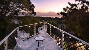 A balcony with white chairs and a table, overlooking a landscape with trees and a distant view. - 3BR Balinese-Style Villa Near Holetown (Holetown)