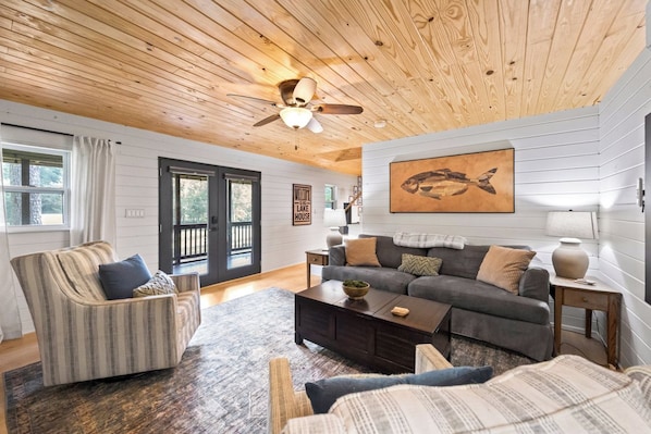 Ein gemütliches Wohnzimmer mit Holzboden, einer Sofagarnitur, einem Couchtisch und einem Bild von Fischen an der Wand.