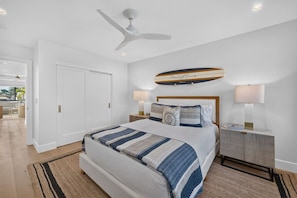 A bedroom with a bed, bedside tables, a ceiling fan, and a wall-mounted surfboard decoration. - Moonlight Dream - 4 Bedroom Panoramic Ocean Views (Encinitas)