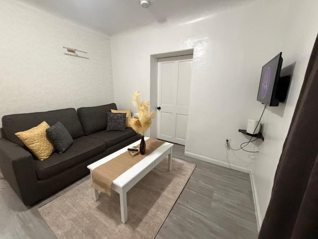 Una sala de estar con un sofá oscuro, una mesa de centro blanca y una puerta blanca.