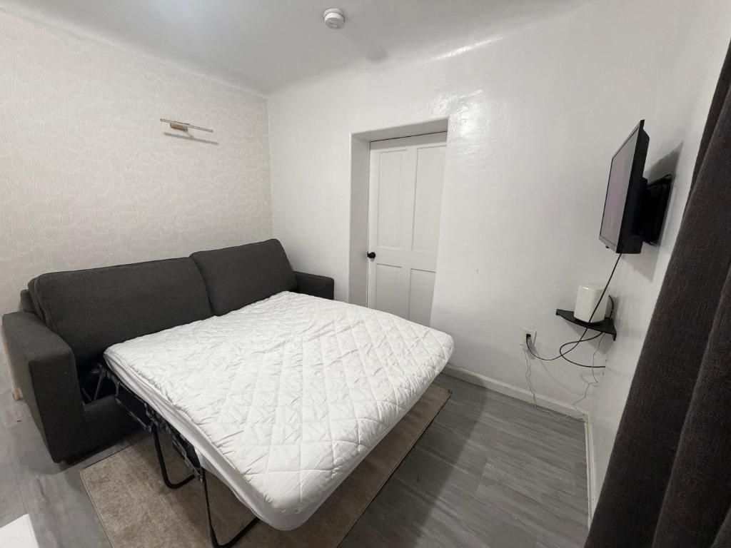 Une petite pièce comprenant un lit, un canapé, une porte et un téléviseur fixé au mur.