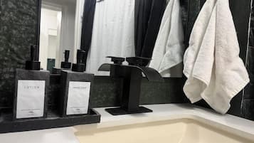 Ein Badezimmer mit einem schwarzen Waschbecken, zwei Flaschen mit der Aufschrift 'LOTION' und 'HANDSEIFE', sowie einem Handtuchhalter mit zwei Handtüchern.