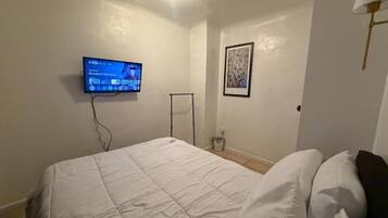 A bedroom with a bed, a television mounted on the wall, a framed picture, and a floor lamp.