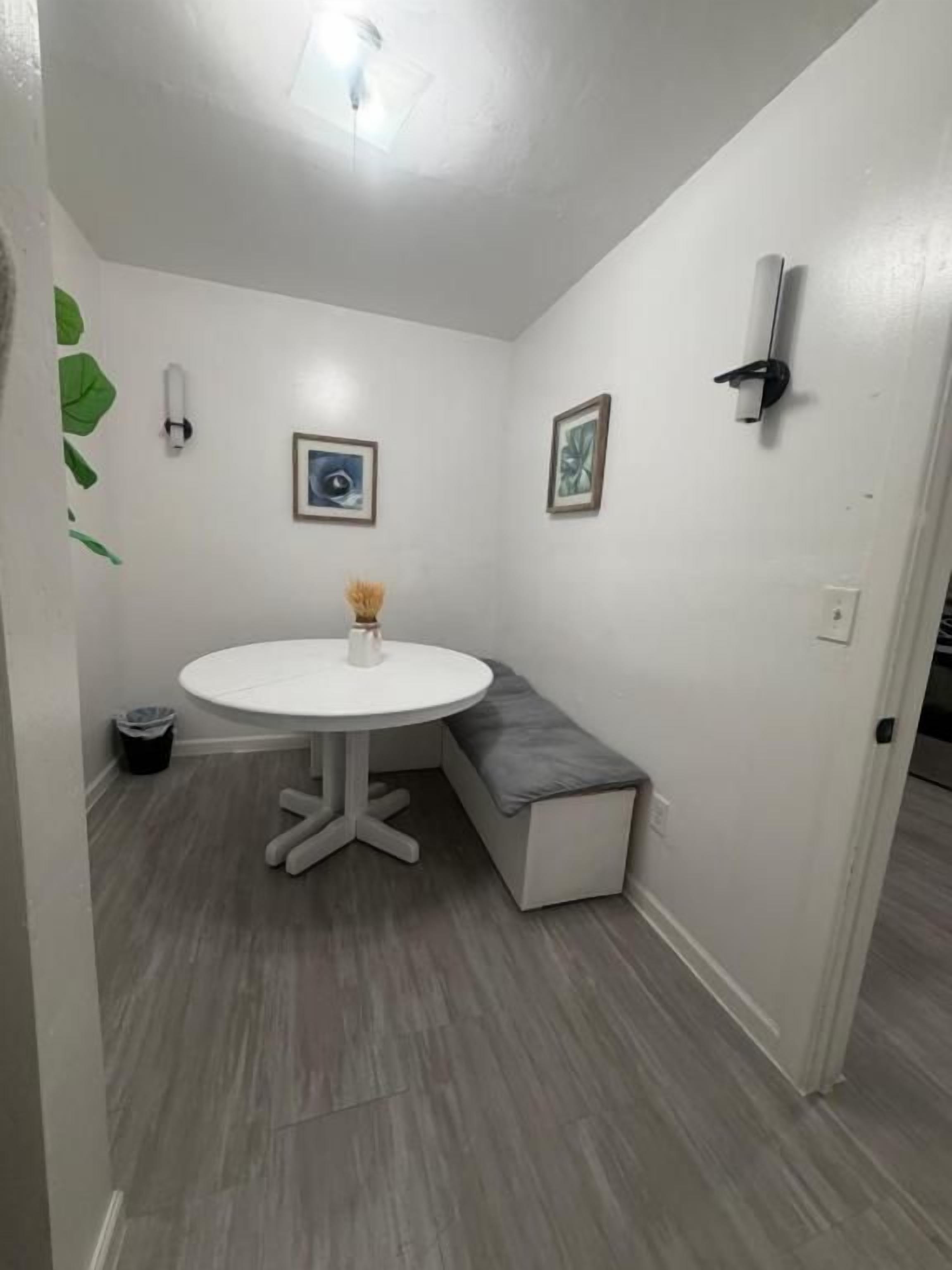 Une petite pièce avec une table ronde, un banc et deux tableaux encadrés accrochés au mur.