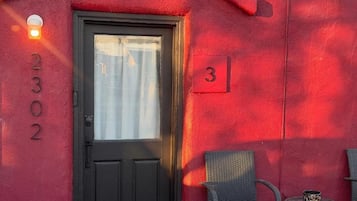 A red building with a black door, a number 3 sign, and a small table with a chair.