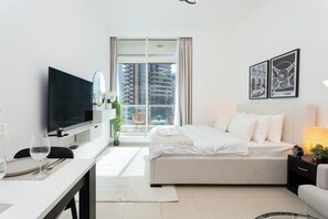A modern hotel room with a bed, a TV, a dining area, and a balcony with a city view. - Tranquil Studio at Botanica (Dubai)