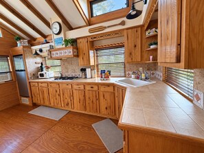 A kitchen with wooden cabinets, a microwave, a sink, and a clock on the wall. - Peaceful Riverfront Cabin with Screened Porch & Fishing! (Live Oak)