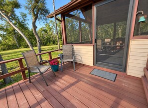 A wooden deck with two chairs and a potted plant, overlooking a grassy area with trees. - Peaceful Riverfront Cabin with Screened Porch & Fishing! (Live Oak)