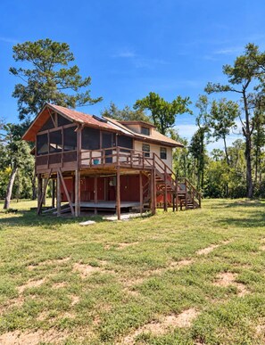Une maison en bois à deux étages, dotée d’un balcon et entourée d’arbres.