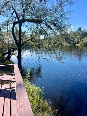 Une terrasse en bois donnant sur une rivière paisible, bordée d’arbres et de verdure.