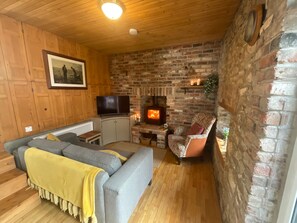 A cozy living room with a fireplace, a sofa, a television, and a brick wall. - Cottage Sleeps 5 with Parking and Garden (Monaghan, County Monaghan,)