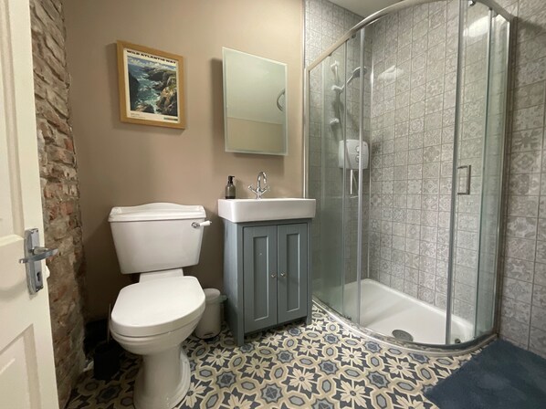 Casa de banho com sanita, lavatório, chuveiro e mosaicos no chão.