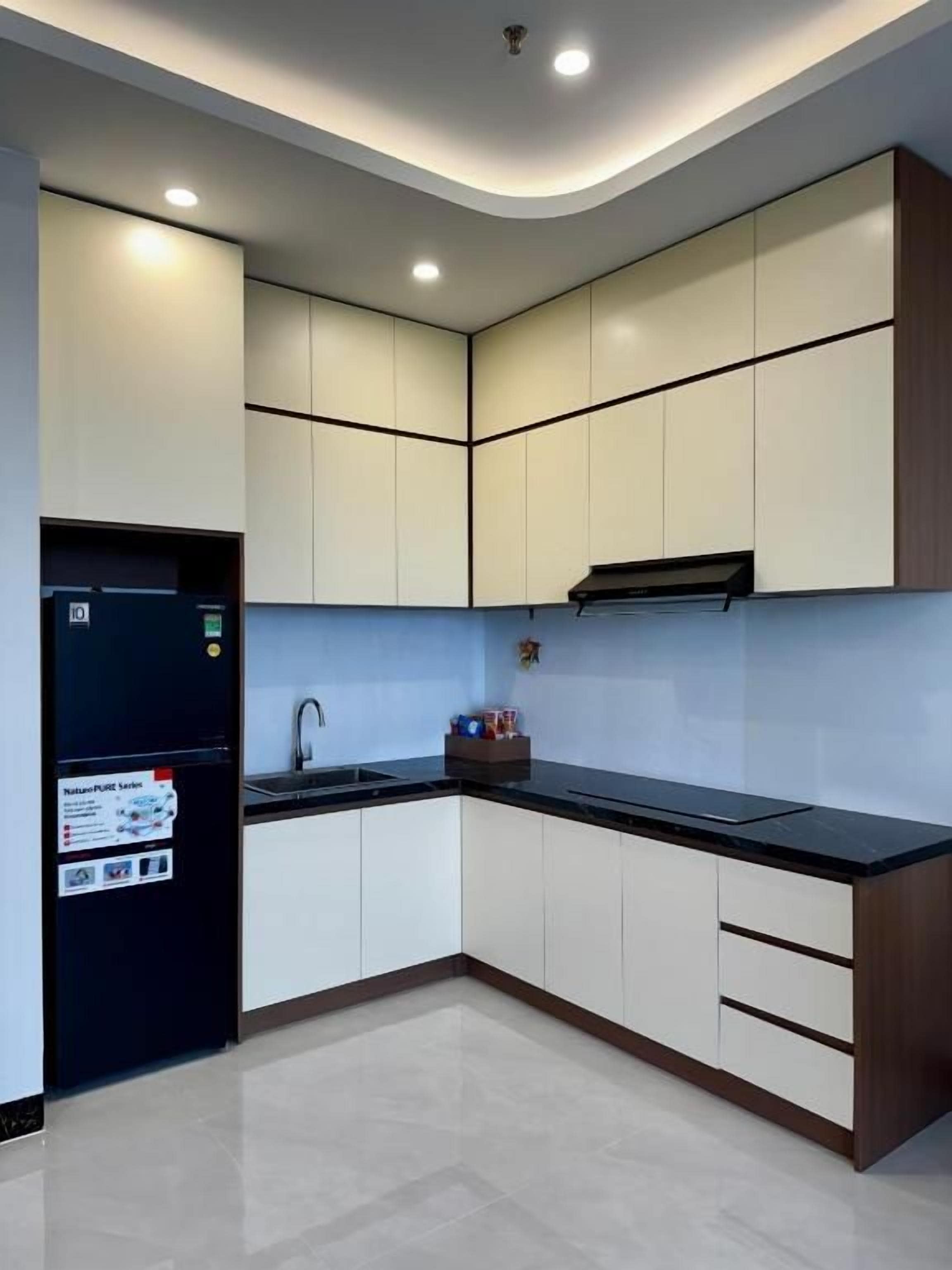 A modern kitchen with a black refrigerator, white cabinets, and a black countertop.