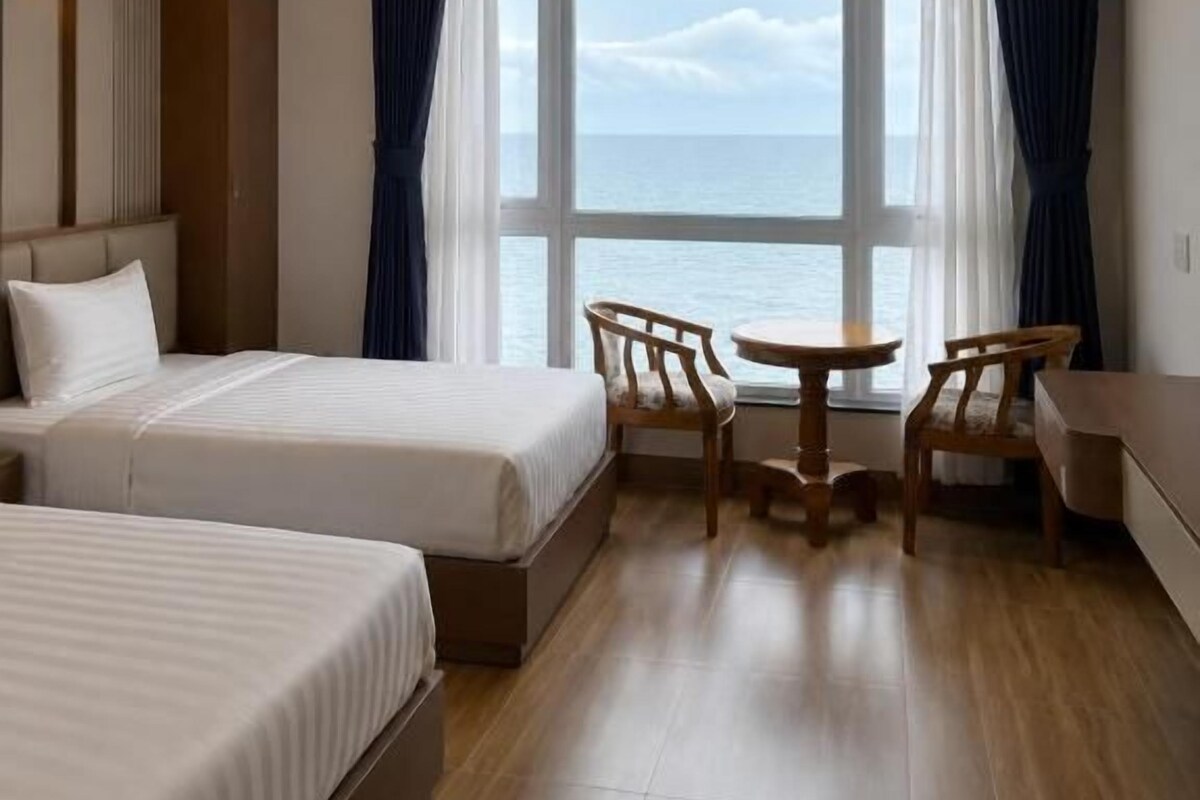 Une chambre d’hôtel avec deux lits, une petite table et vue sur la mer.