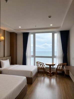 Une chambre d’hôtel avec deux lits, une petite table et vue sur la mer.