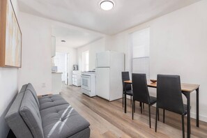 A modern kitchen with white appliances, a dining area with a wooden table and black chairs, and a grey sofa in a bright room with wooden flooring. - The University District Hideaway | Spacious 3BR (Salt Lake City)