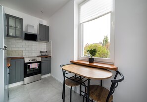 A modern kitchen with grey cabinets, a built-in oven, and a window with a view of trees. - Metro Politechnika Central Apartment (Warszawa)