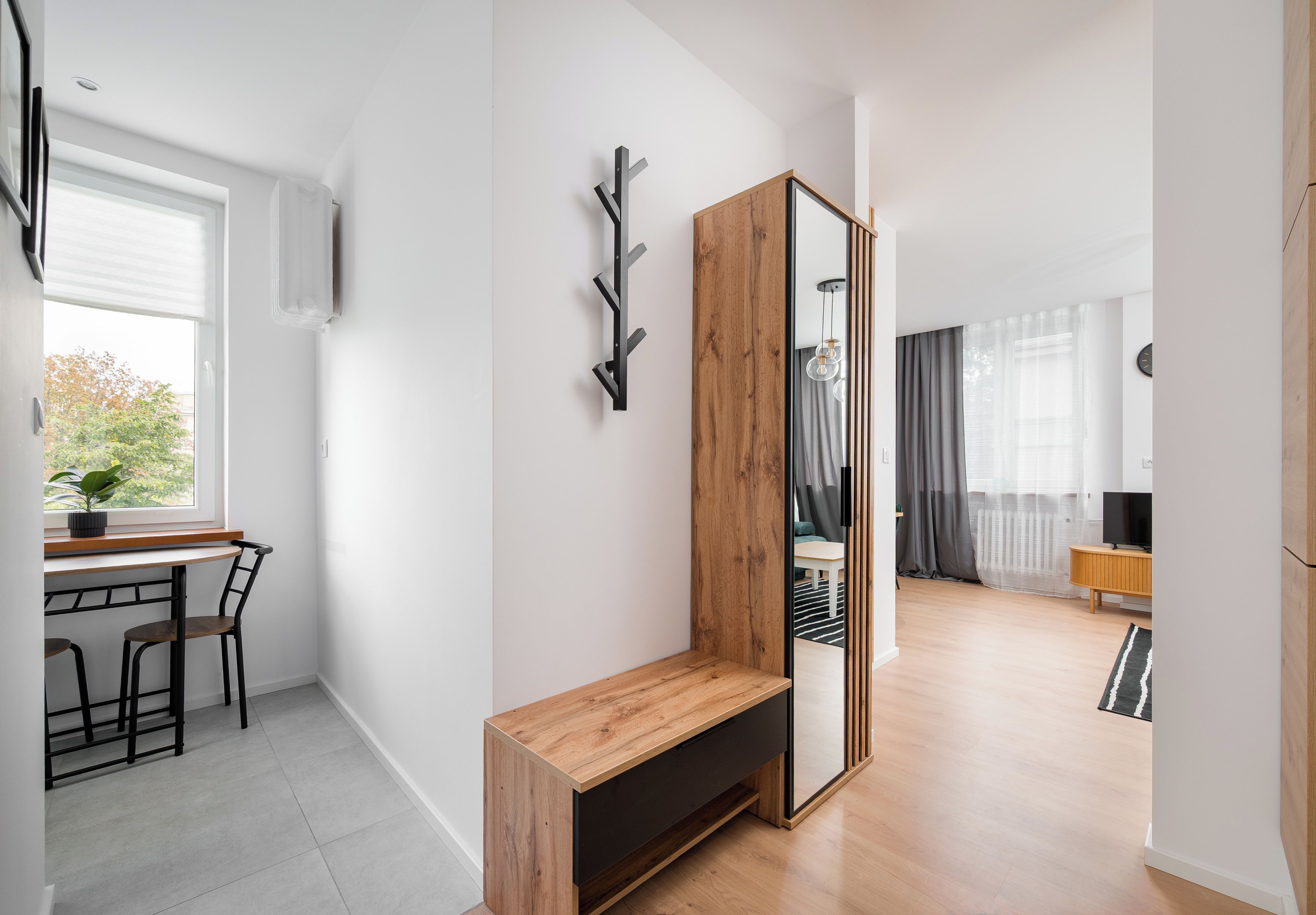 A modern living room with a wooden bench, a large mirror, and a dining area with a table and chairs.