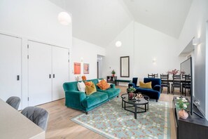 A modern living room with a teal sofa, a blue sofa, and a dining area with a black table and chairs. - Luxury London Living 3BR 3BA Zone 1 (London)
