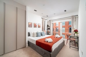 A modern bedroom with a bed, a small table with chairs, and a balcony with a view of buildings. - Luxury London Living 3BR 3BA Zone 1 (London)