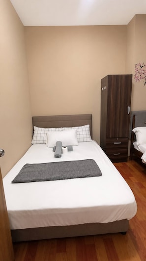Ein ordentlich bezogenes Bett mit einer grauen Tagesdecke, ein Holzschrank und eine Wand mit einer Blumensticker.