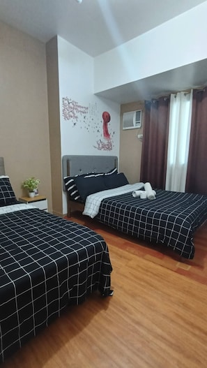 Habitación de hotel con dos camas, aire acondicionado instalado en la pared, una ventana con cortinas y un adorno en la pared.