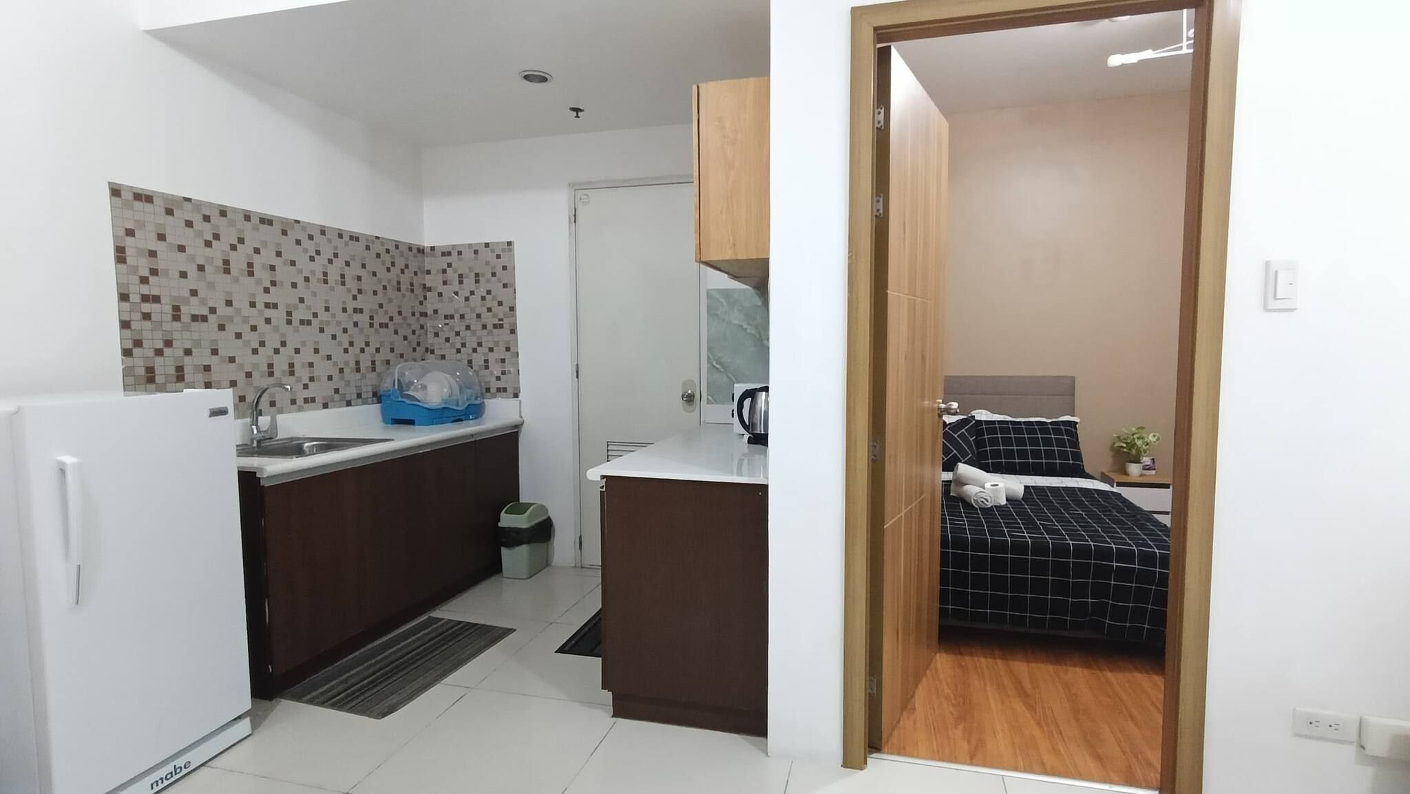 A compact kitchen with a refrigerator, sink, and a tiled backsplash.