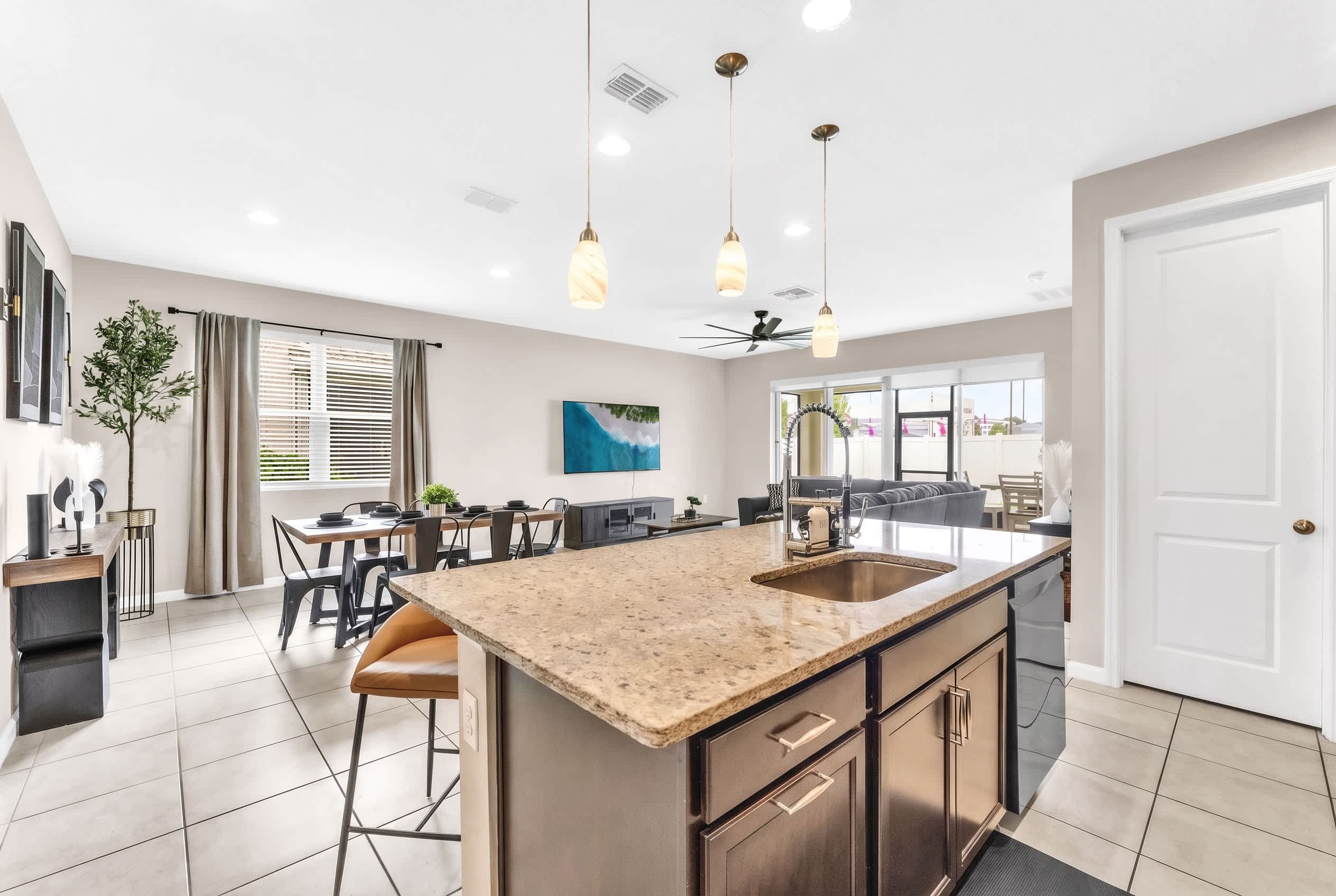A modern kitchen with a central island, bar stools, and a dining area with a table and chairs.