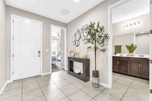 A hallway with a white door, a fireplace with decorative items, a mirror, and a plant. - Sunshine & Stay Awhile (Davenport)