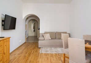 A living room with a flat-screen TV mounted on the wall, a sofa with cushions, a wooden cabinet, and a rug on the floor. - Nowolipki Serene Apartment (Warszawa)