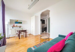 Ein modernes Wohnzimmer mit einem grünen Sofa, einem Esstisch mit Stühlen und einem durch einen offenen Durchgang einsehbaren Küchenbereich.