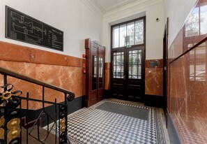 A hallway with a checkered floor, a fire alarm, and a door with a green exit sign. - Dietla Avenue Homely Apartment (Kraków)