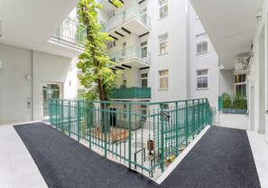 Un immeuble résidentiel à plusieurs étages doté d’une cour intérieure, de balcons ornés de verdure et d’un arbre.