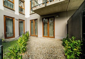 A courtyard with a gravel path, wooden-framed windows, and a metal fence. - Posnania Navy Blue Apartment (Poznań)