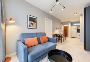 A modern living room with a blue sofa, orange cushions, a black floor lamp, and a framed picture on the wall. - Posnania Navy Blue Apartment (Poznań)