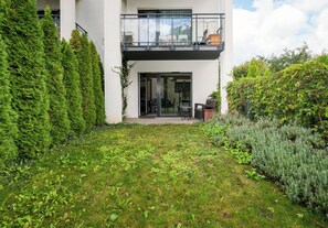 A modern two-story building with a balcony, a glass door entrance, and a well-maintained garden with various plants. - Kołacińska Riverside Comfort Apartment (Warszawa)