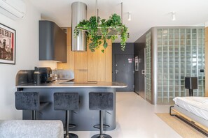 A modern kitchen with a central island, bar stools, a hanging plant, and a glass partition wall. - Sokolska Towers Studio 92 (Katowice)