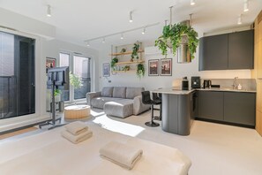 Ein zeitgemäßer Wohnraum mit Sofa, Couchtisch und Küchenbereich mit Arbeitsplatte und Geräten.