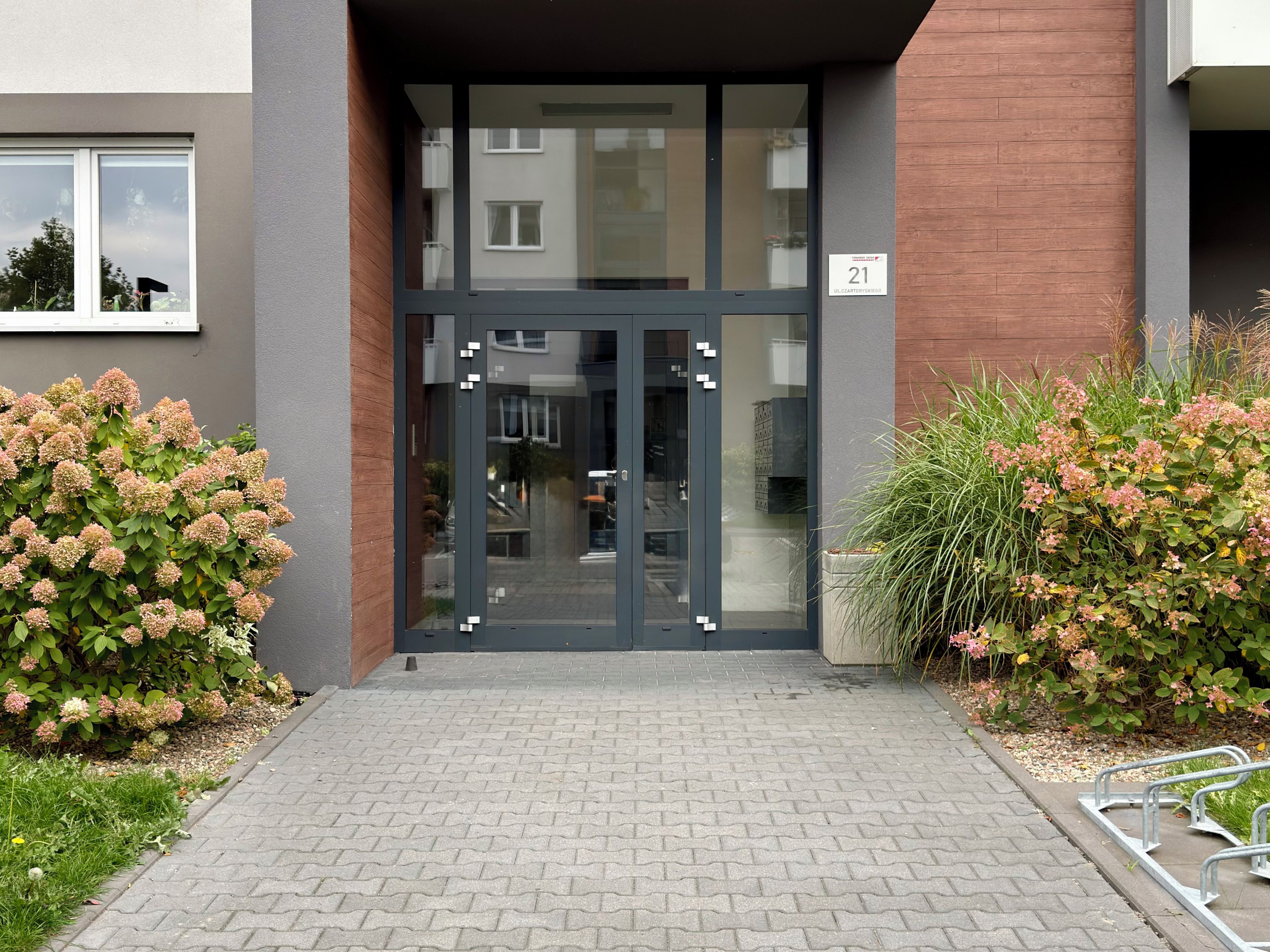 Une entrée moderne avec une porte en verre, un mur en briques et une plaque numérotée.