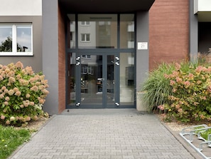 A modern building entrance with a glass door, a brick wall, and a number plaque. - Czartoryskiego Modern Apartment (Wrocław)