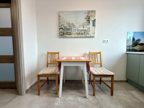 A dining area with a table and two chairs, a painting on the wall, and a cabinet to the right. - Czartoryskiego Modern Apartment (Wrocław)