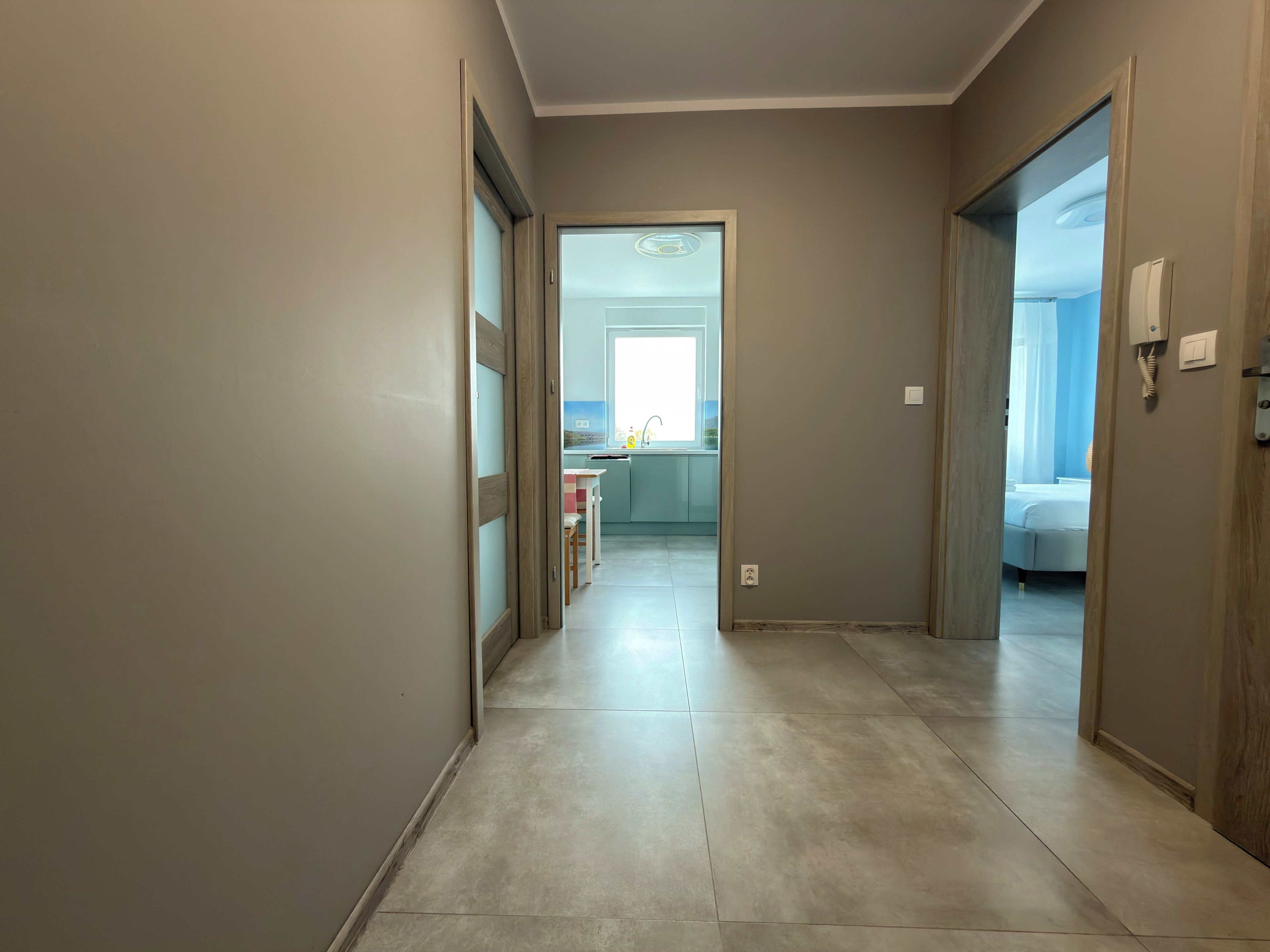 Un couloir menant à une chambre et à une salle de bain, avec une cuisine visible au fond.