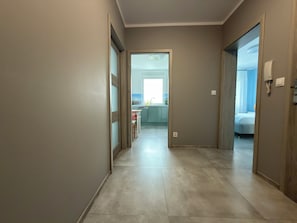 Un couloir menant à une chambre et à une salle de bain, avec une cuisine visible au fond.
