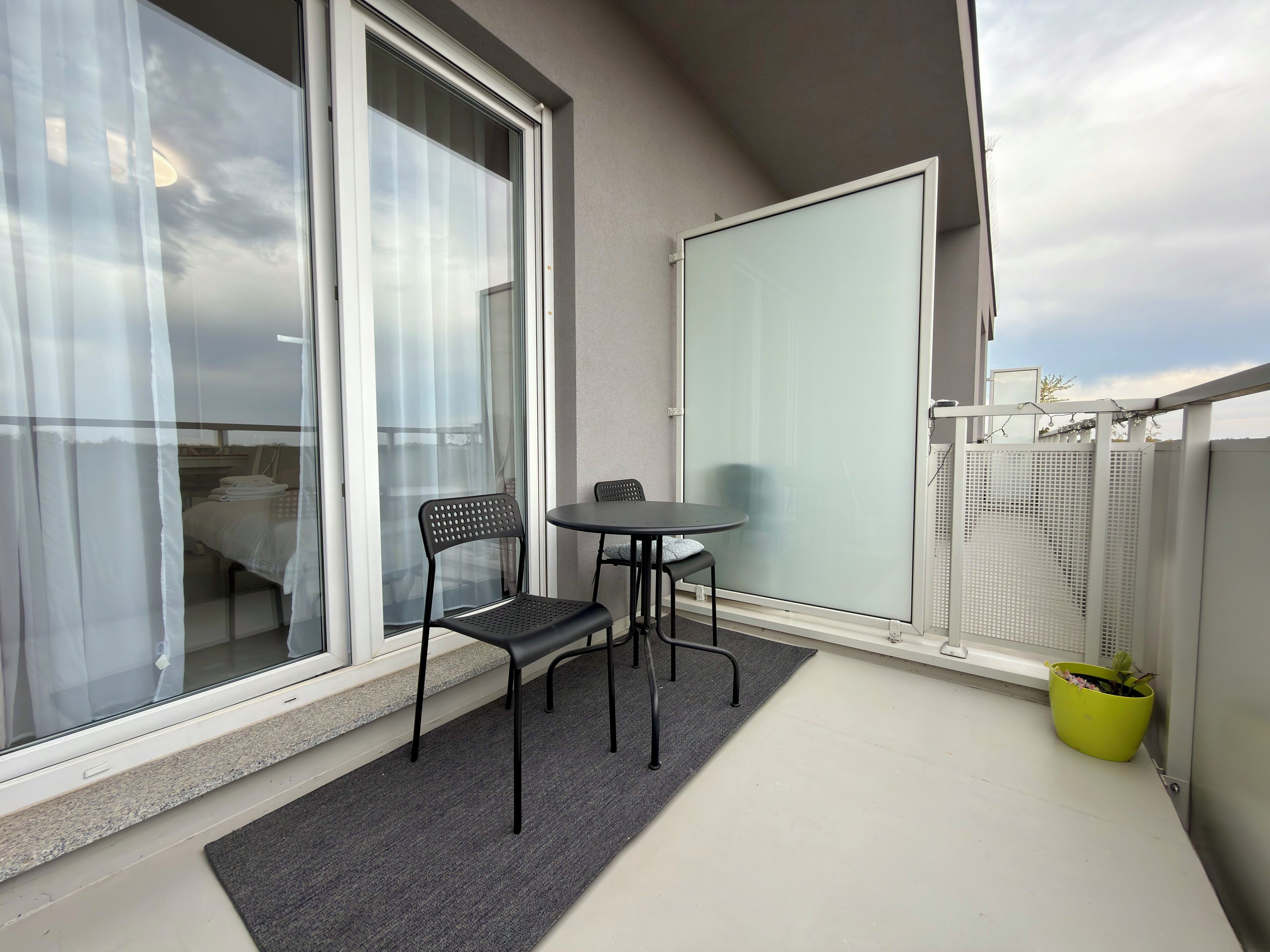 Un balcon avec une chaise, une petite table et un pot de fleurs.