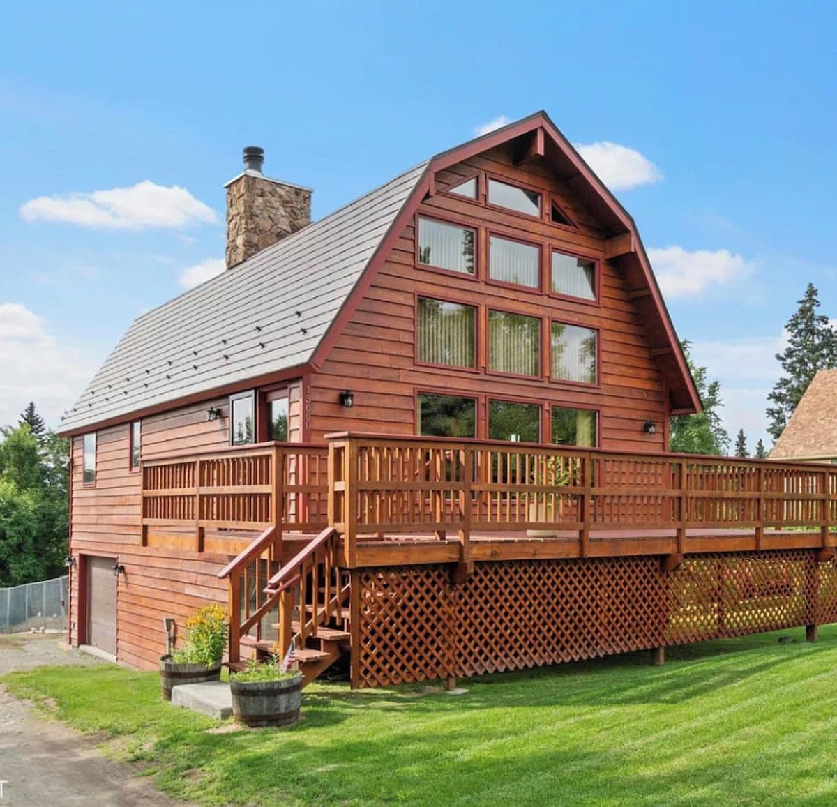 A two-story wooden cabin with a sloped roof, a balcony with a wooden railing, and a chimney.