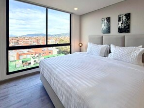 A bedroom with a large bed, a view of the city, and two wall-mounted artworks. - New Listing (Bogotá)